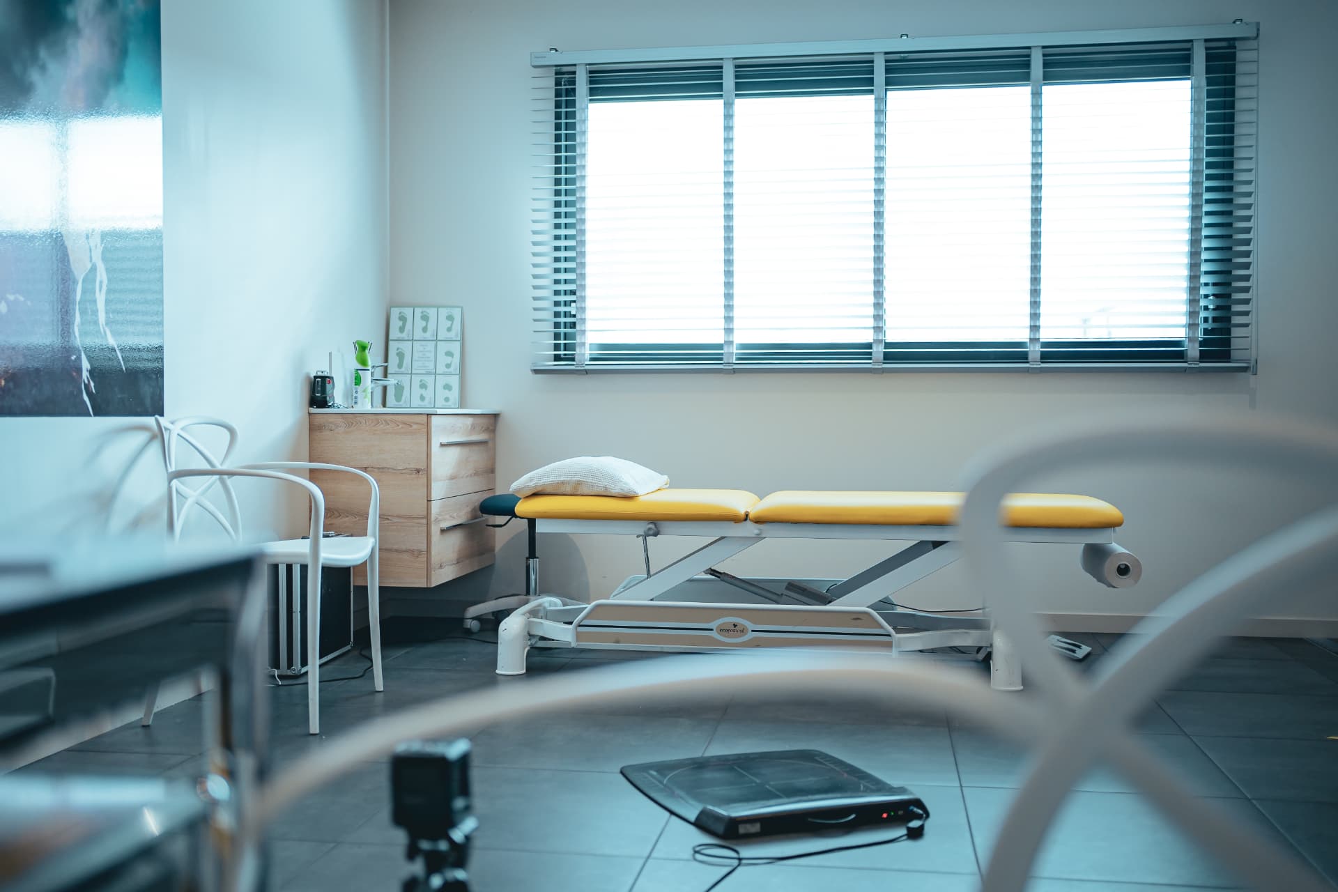 Salle d'examen podologique avec table de soins et plateforme de posturologie